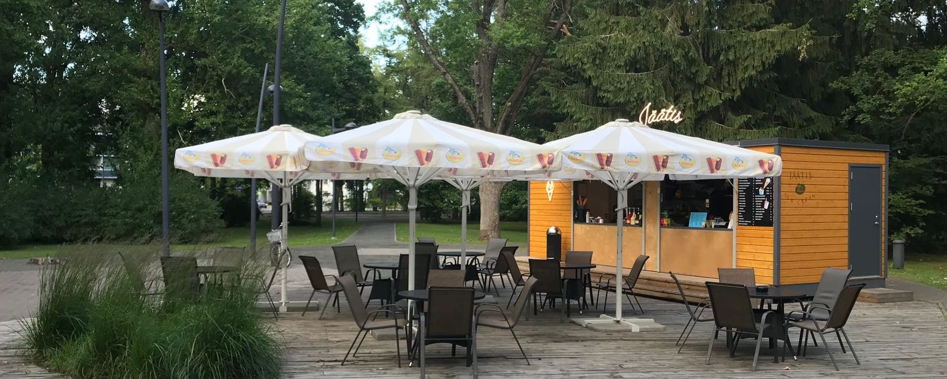 Valkoinen ulkokatoksen varjostin punaisen ja keltaisen kuvioinnilla puistossa oranssisen kahvion