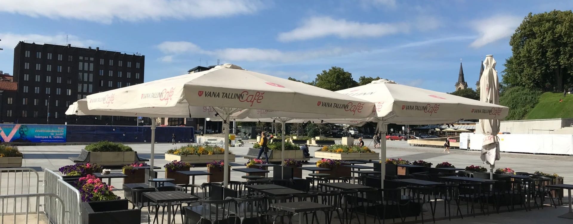 Suuret beigit aurinkovarjot Vana Tallinn Café -ravintolan terassilla, mustat tuolit ja kukat