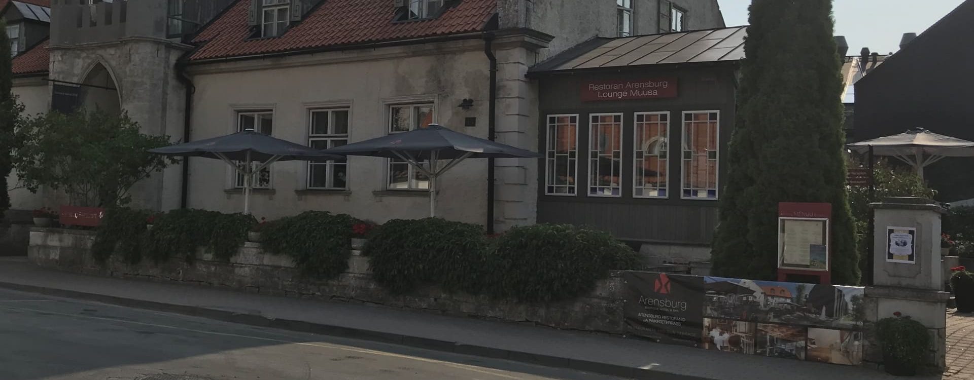 Kaksi laajalti levinnyttä tummansinistä aurinkovarjoa ravintola-alueen pöytien yllä harmaan kiven