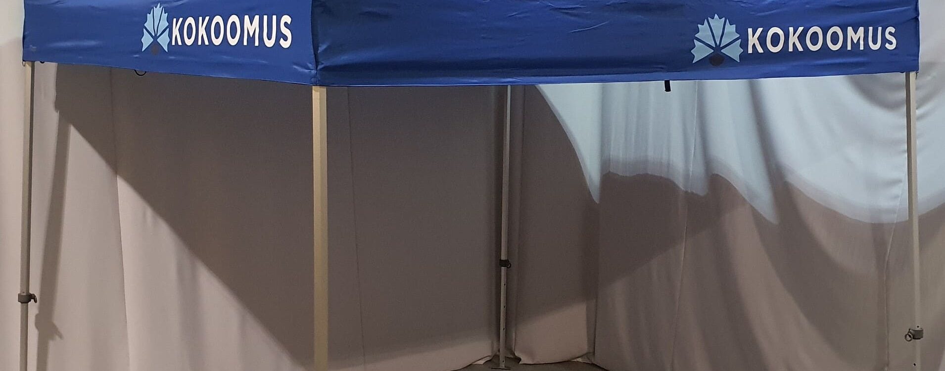 Sininen Kokoomus-teltta sivuverhoilla sisätiloissa, neliönmuotoinen, kattaa kokouksen tai