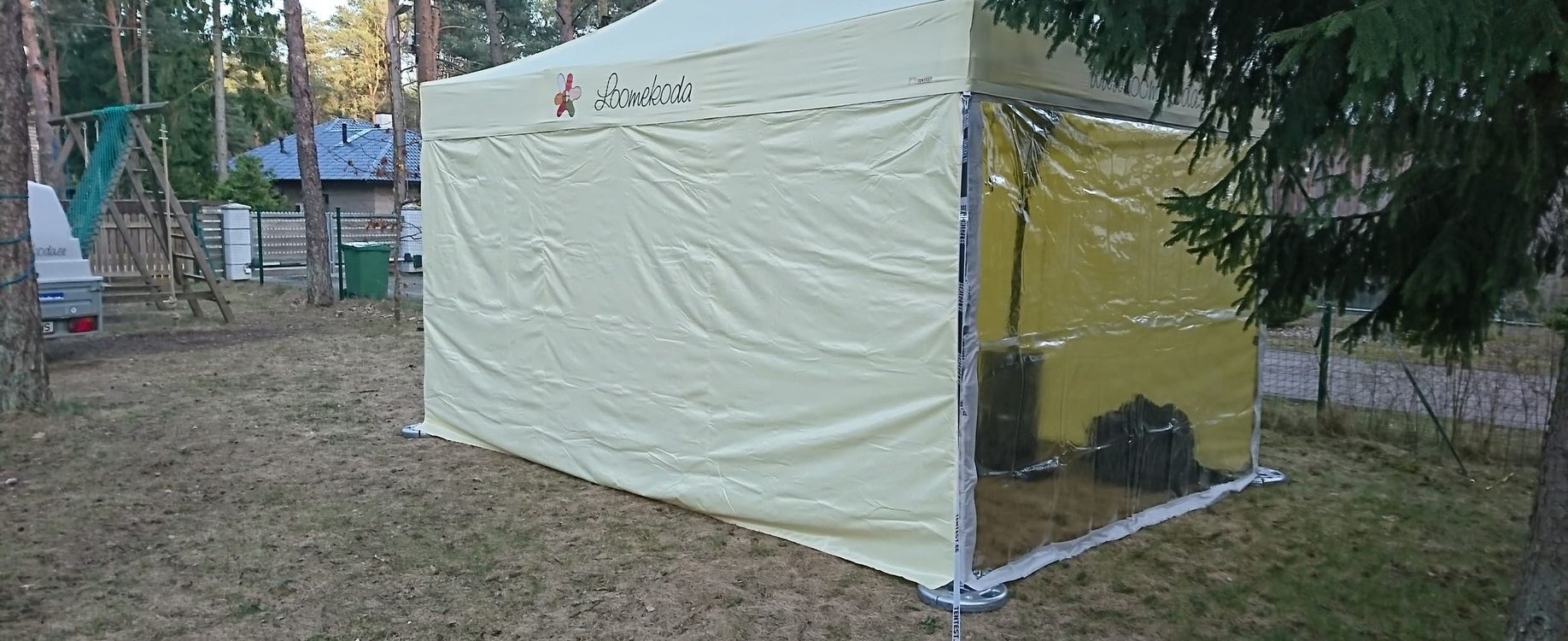 Lomakoda teltta valkoisella katolla ja keltaisilla sivuseinillä metsän keskellä leirintäalueella