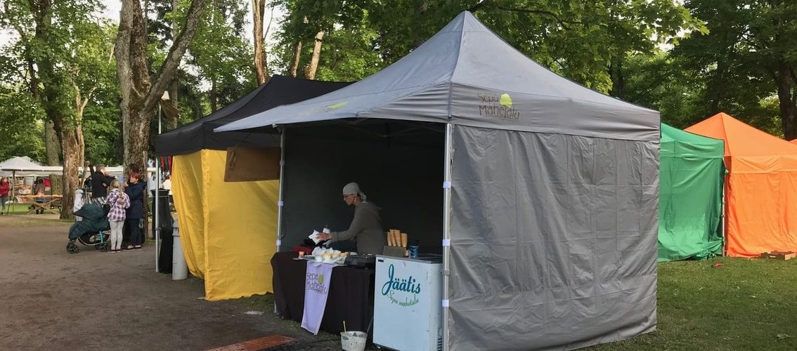 Harmaa telttakatos ulkotapahtumassa, jonka sisällä mies myy ruokaa.