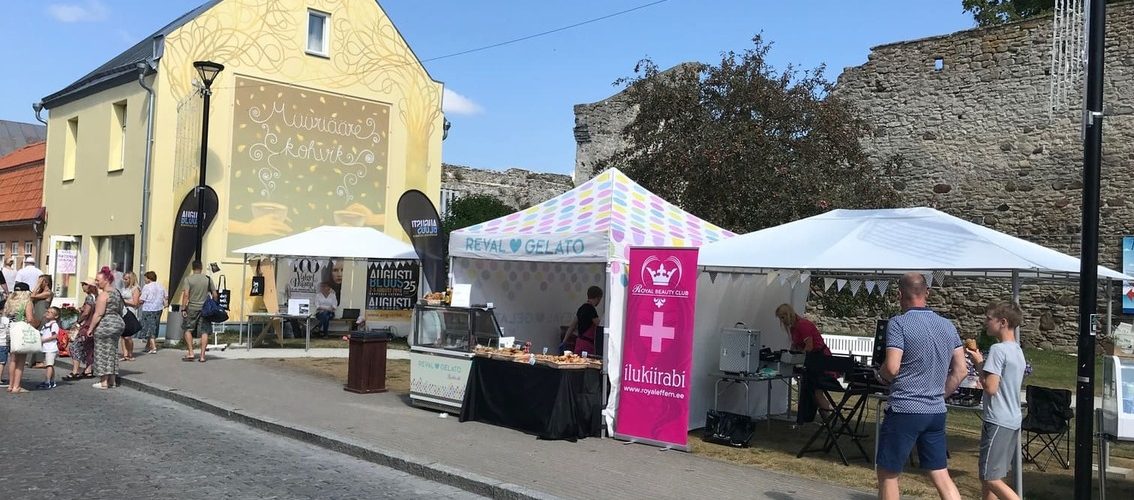 Ulkoilmatapahtuma keskiaikaisen linnoituksen edessä. Keltainen talo, valkoisia telttoja, ihmisiä