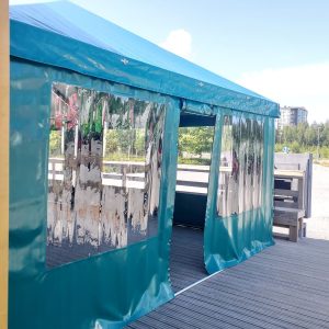 Sininen teltta-mainos puusta rakentamalla kannella, jossa näkyy kaupunkimaisemaa ja puita taustalla