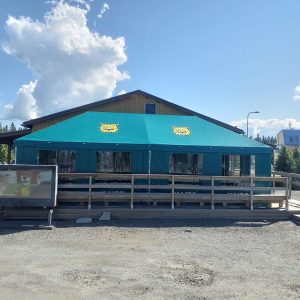 Turkoosi värisellä kangaskatolla varustettu ravintola tai kahvila puisella terassilla.