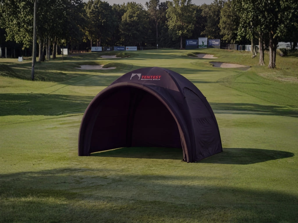 Tumma ilmatäytteinen Tentest-tapahtumateltta kaarevalla futuristisella muotoilulla vihreällä golfkentällä