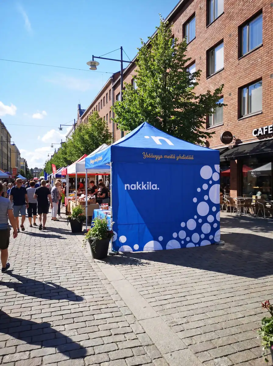 Sininen nakkila-teltta markkinoilla katuympäristössä, jossa näkyy valkoisia pisteillä koristeltuja
